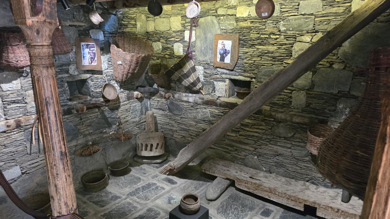 Traditional Kalash grinding stone, woven baskets and household tools inside a stone-walled museum room