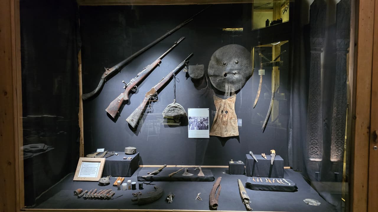Historic Kalash rifles, daggers, shields and hunting tools displayed in a museum case