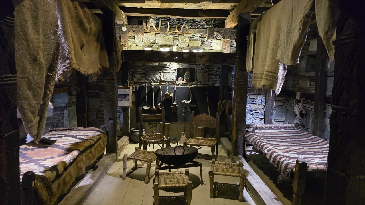 Kalash hearth room showing hanging textiles, hand-woven bedding and carved wooden pillars